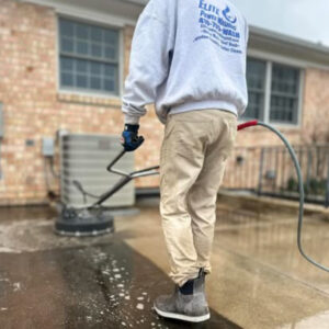 Man power washing a concrete surface with a surface cleaner attachment. The man is wearing work boots and a grey sweatshirt with "Elite Power Washing" printed on the back. Power washing is an effective alternative to spray paint.